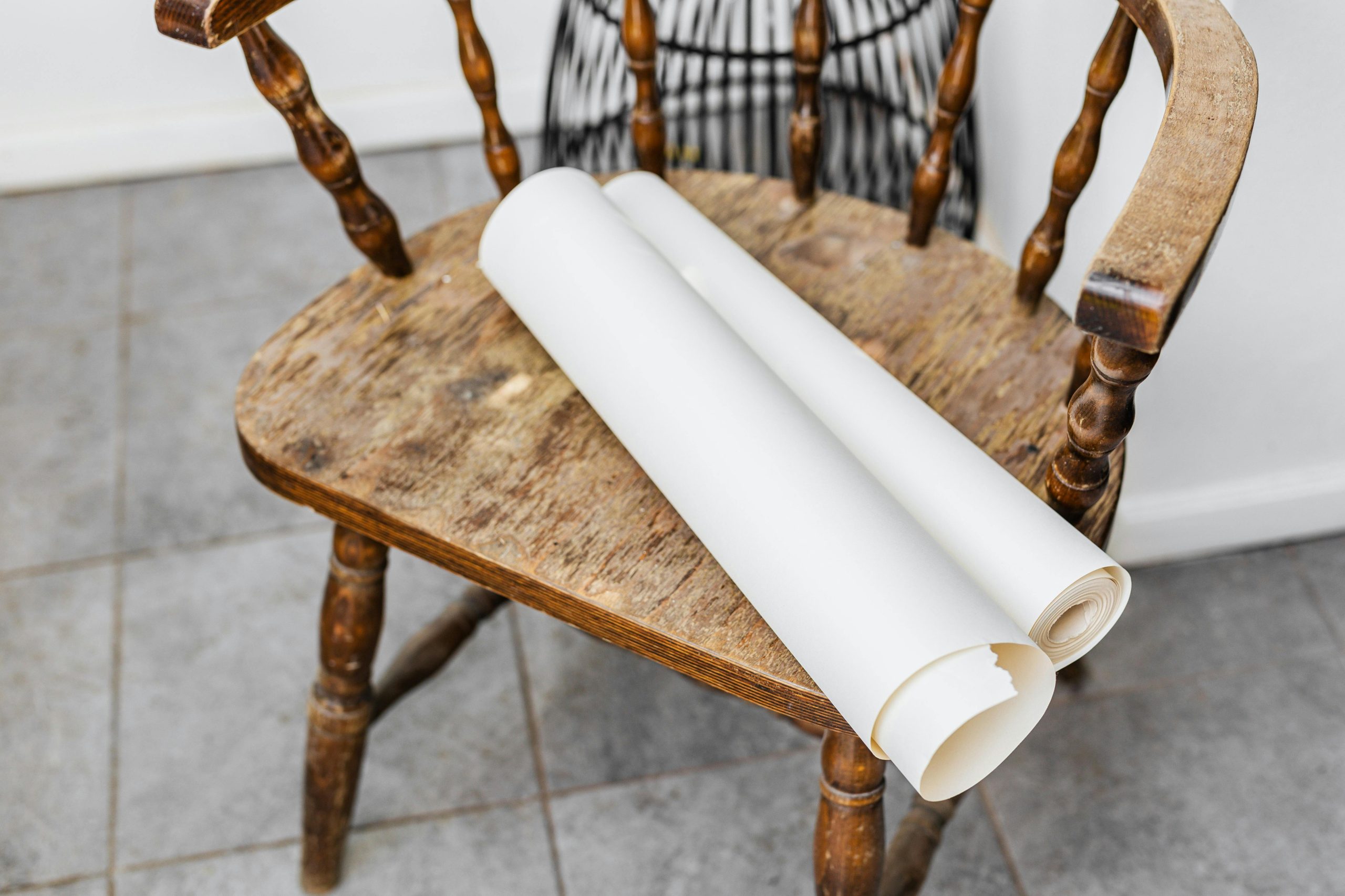 An antique wooden chair with rolled paper on a tiled indoor floor, capturing a vintage essence.